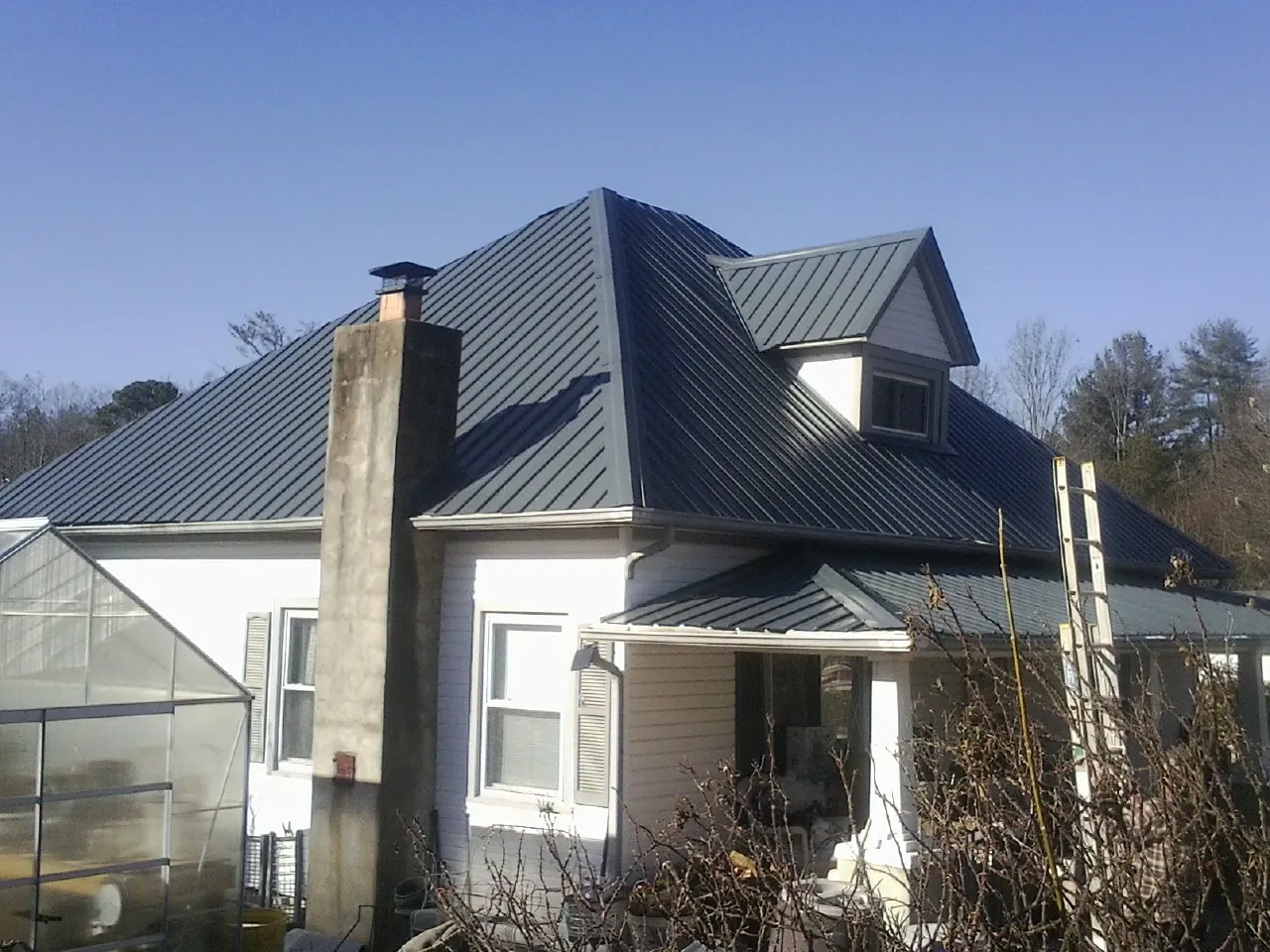 Dark blue standing seam metal roof on a white farmhouse with dormer — Slate & Tile Roof Repair by Roofing Brothers in Benton