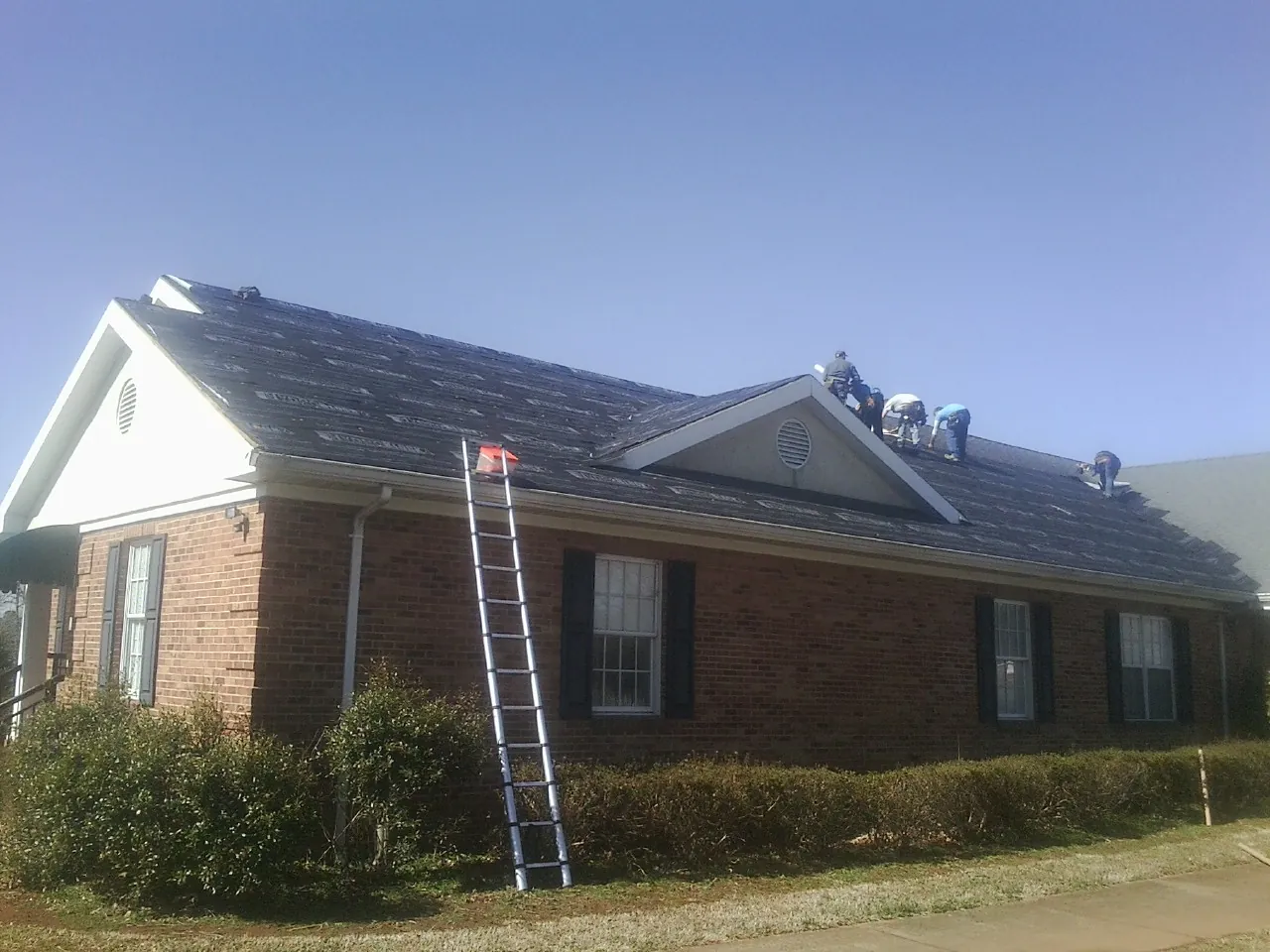 Crew tearing shingles off a brick ranch roof with a ladder set — Metal Roof Repair work by our crew in Benton